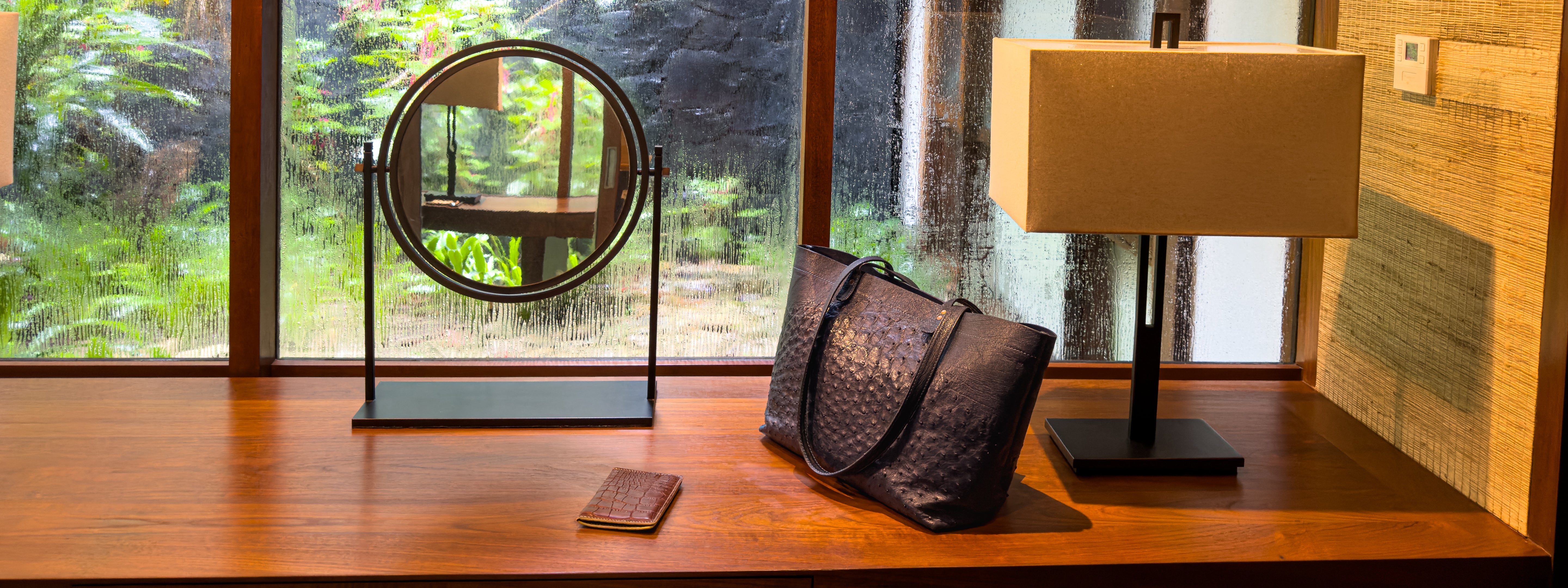 Black handbag on a wooden surface with a lamp and mirror in the background