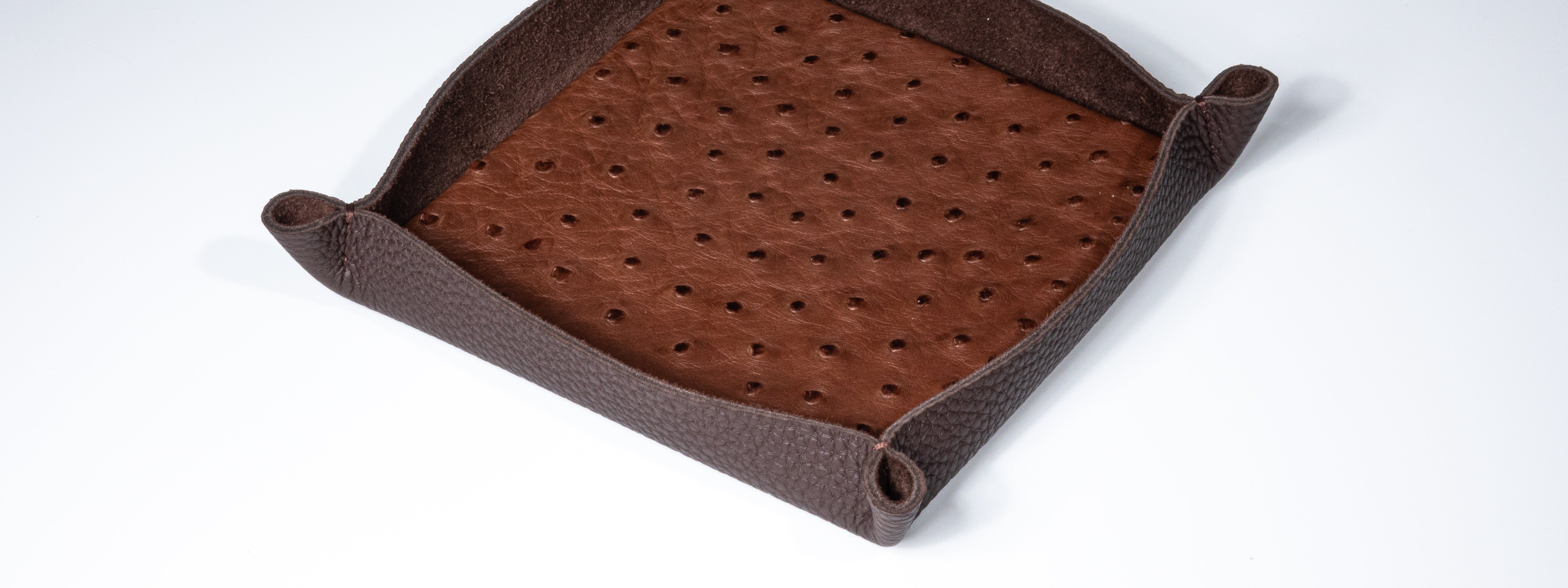Brown leather dice tray with perforated design on a white background